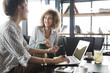 © Cavan Images - Businesswoman working on laptop while sitting by happy colleague at cafe