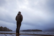 Man Looking At River While Standing On Jetty Against Cloudy Sky