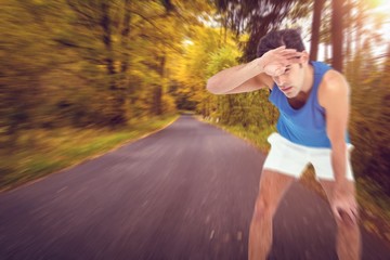 Wall Mural - Tired athlete wiping his sweat with hand against country road along trees in the lush forest