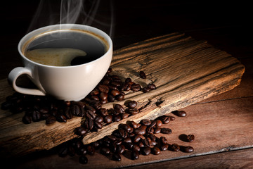 Wall Mural - Steaming coffee cup and coffee beans on wood background with copy-space and dark tone.