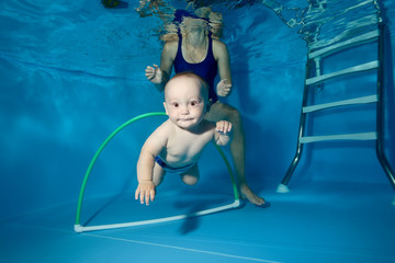 A little boy trains in the pool underwater, swims through the Hoop