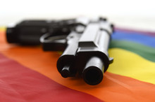 Still Life With Close Up Gun Resting On Gay Parade Flag Representing Sexual Discrimination And Intolerance