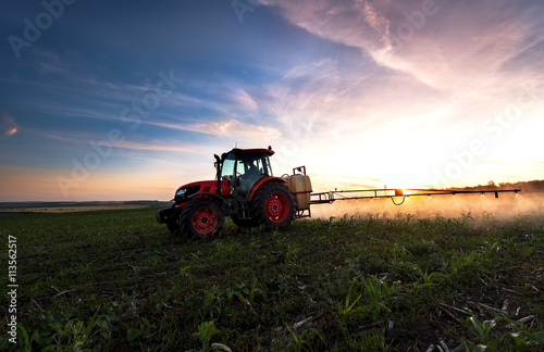Fotografía Tractor pulverizando un campo en la granja en la primavera, la agricultura