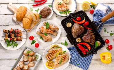 Mixed Grilled meats with vegetables on a white wooden table.