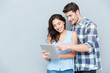 © Drobot Dean - Young couple pointing at pc tablet over gray background