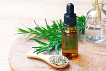 A Bottle Of Rosemary Aromatherapy Oil Extract With Fresh And Dried Rosemary Leaf On Wooden Spoon.