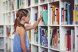 © WavebreakMediaMicro - School girl taking a book from bookshelf in library