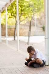 Wall Mural - Sad schoolboy sitting alone in corridor