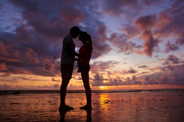 Wall Mural - sunset silhouette of young couple in love hugging at beach
