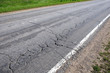 Suburban road in bad condition needs repairs. Rural car road with broken asphalt in sunny summer day diagonal view