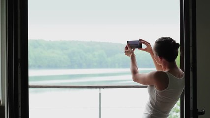 Wall Mural - Silhouette of woman photographing lake from the window 