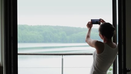 Wall Mural - Silhouette of woman photographing lake from the window 