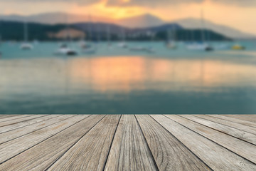 Wood table top with blurred sunset on the beach and sailing boat background