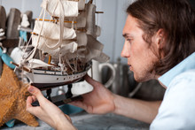 Young Man Looks At Model Of Sailing Ship In Vintage Interior