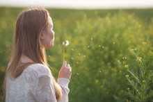 Young Spring Fashion Woman Blowing Dandelion In Spring Garden. Springtime. Trendy Girl At Sunset In Spring Landscape Background. Allergic To Pollen Of Flowers. Spring Allergy.