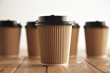 Wall Mural - One focused craft paper coffee cup with black cap isolated in center in front of unfocused group of others on vintage brushed pallet table close view