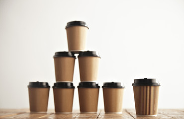 Wall Mural - One cup presented in focus in front of craft cardboard take away paper cups with black caps in pyramid house shape isolated on handmade pallet wooden table