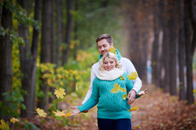 Husband And Pregnant Wife Are Walking In Autumn Park