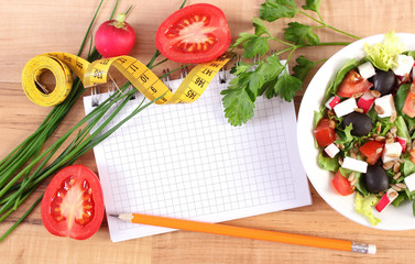 Fresh greek salad with vegetables, centimeter and notepad for writing notes, healthy nutrition and slimming concept