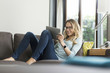 © Westend61 - Smiling woman at home on couch using digital tablet