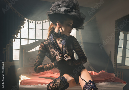 Fototapeta na szkło Girl in retro hat and lace lingerie on a bed with pink sheets