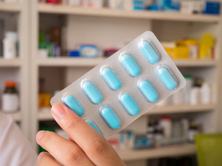 pharmacist showing medicine pills with pharmacy shelves backgrou