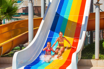 Wall Mural - Two different ages children at aquapark slide down water slide. Summer aquapark holiday. Outdoor water slide.