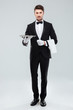 © Drobot Dean - Confident young waiter in tuxedo standing and holding tray