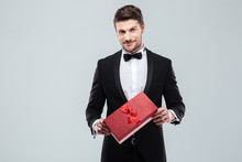 Confident Attracive Man In Tuxedo Standing And Holding Gift Box