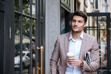 Man with coffee and newsaper walking along street in city