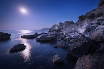 Wall Mural - Colorful night landscape with full moon, lunar path and rocks in summer. Mountain landscape at the sea.