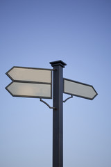 Signpost. Index path, located on the pole. Black metal pole. Arrows with a white field for writing. Against the background of the blue sky.