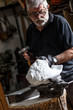 Senior sculptor working on his marble sculpture in his workshop with hammer and chisel
