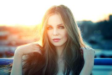 Wall Mural - Outdoor portrait of young pretty sexy woman with magic eyes posing at roof at the end of bright sunset. Lovely soft back light.