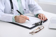 © rogerphoto - Close-up of a female doctor filling  out application form , sitting at the table in the hospital