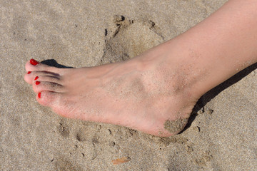 Woman feet with red pedicure walking on the hot sand of the beac