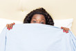 young woman looking from under the covers.