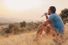 Athletic Man In His 30s Resting And Drinking Water From A Bottle While Sitting Down Outdoor