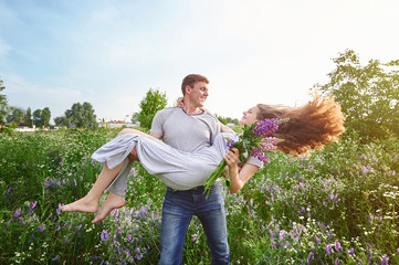 Happy love man holding a woman on his arms in field