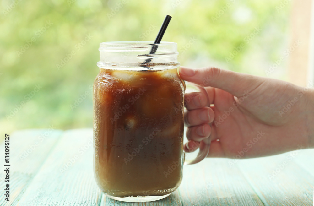 Glass jar of iced coffee on blurred natural background