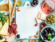 Summer wine snack set. Glass of rose, meat, cheese, olives, honey, bread sticks, nuts, capers and berries with white ceramic board in center, blue wooden background