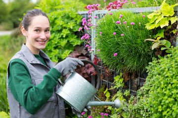 Young attractive woman working in a public garden watering flowe