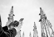 Businessman Using Mobile Phone With Telecommunication Towers With TV Antennas And Satellite Dish, Black And White
