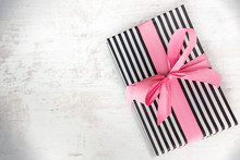 Gift Box Wrapped In Black And White Striped Paper With Pink Ribbon On A White Wood Old Background