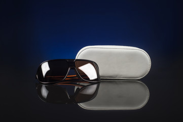 Elegant sunglasses and case on black background with blue light