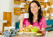 © Fotos 593 - Pretty brunette woman sitting at table inside bakery, holding cup of coffee and smiling happily, bread selection in front