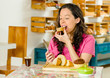 © Fotos 593 - Pretty brunette woman wearing pink shirt sitting at table inside bakery, biting into slice of bread