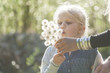 Blond little girl blowing seeds of an umbel into the air with helping hand of her mother
