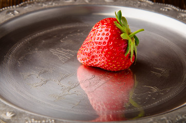 Single tasty red strawberry on a vintage plate closeup