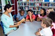 © WavebreakMediaMicro - Teacher reading a book to mixed race children